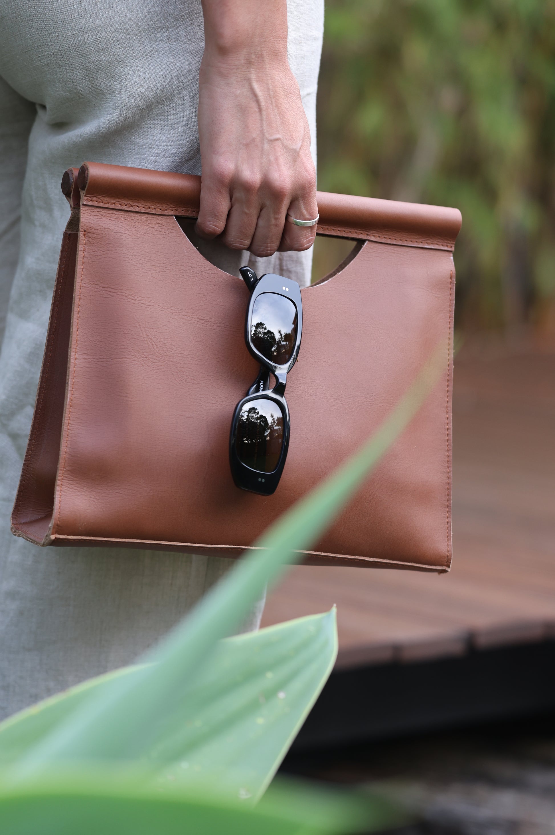 Elegant brown leather clutch bag with natural wooden handle, showcasing clean lines and artisan craftsmanship.