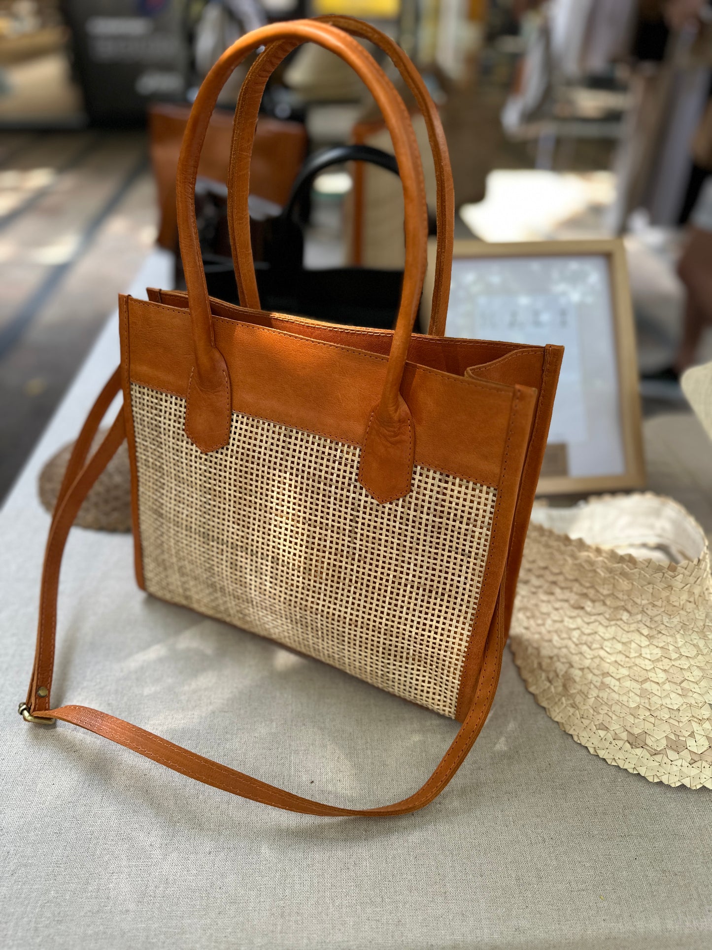 Rome Rattan Handbag in tan cowhide leather and natural rattan with dual handles, adjustable crossbody strap, small interior pocket, and secure zipper closure. Lightweight, compact, and perfect for everyday elegance.