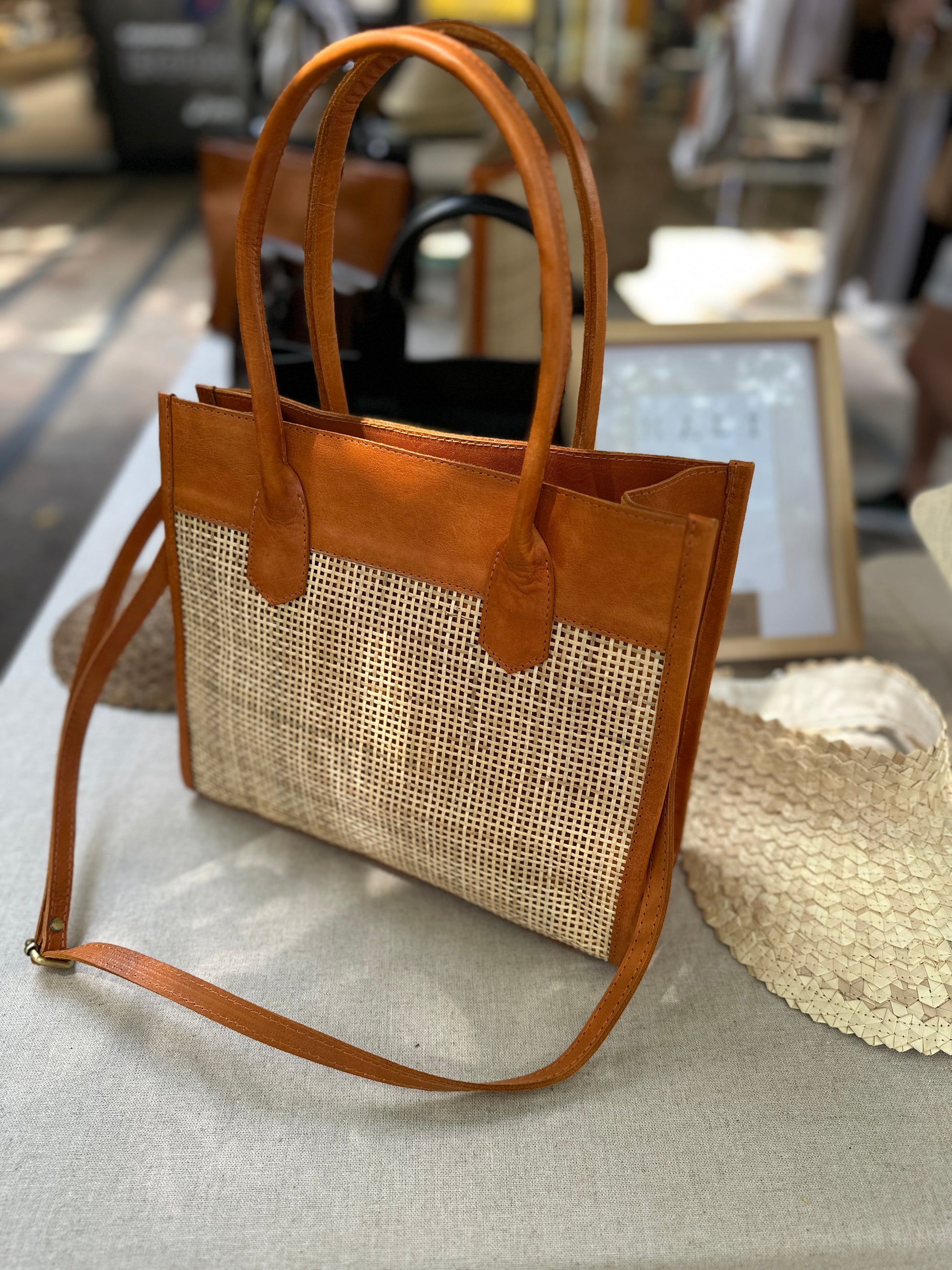 Rome Rattan Handbag in tan cowhide leather and natural rattan with dual handles, adjustable crossbody strap, small interior pocket, and secure zipper closure. Lightweight, compact, and perfect for everyday elegance.