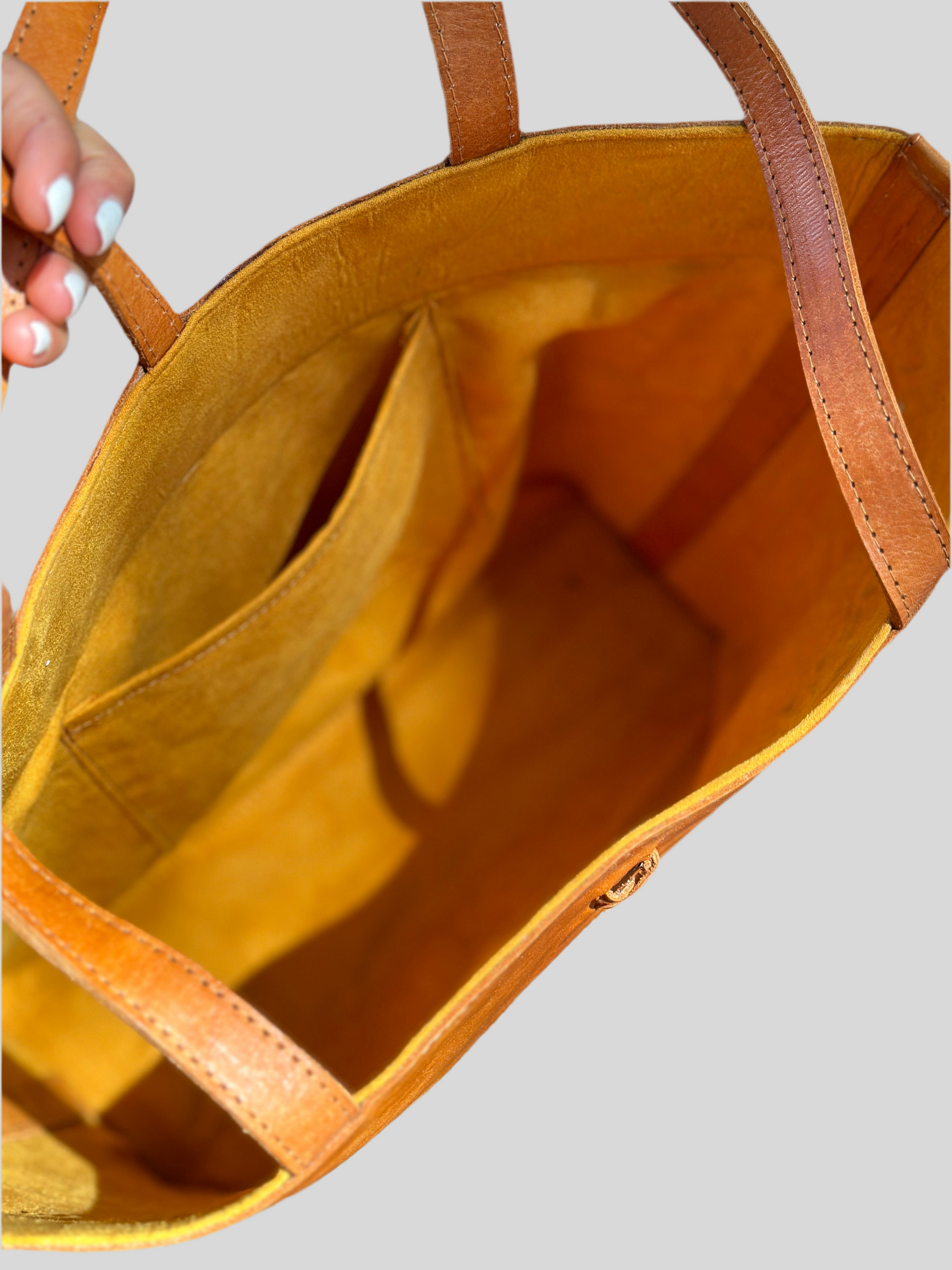 inside view of the Handmade Venice rattan tote bag featuring camel-toned leather straps and natural rattan body. Unique strap closure for a chic and secure look.