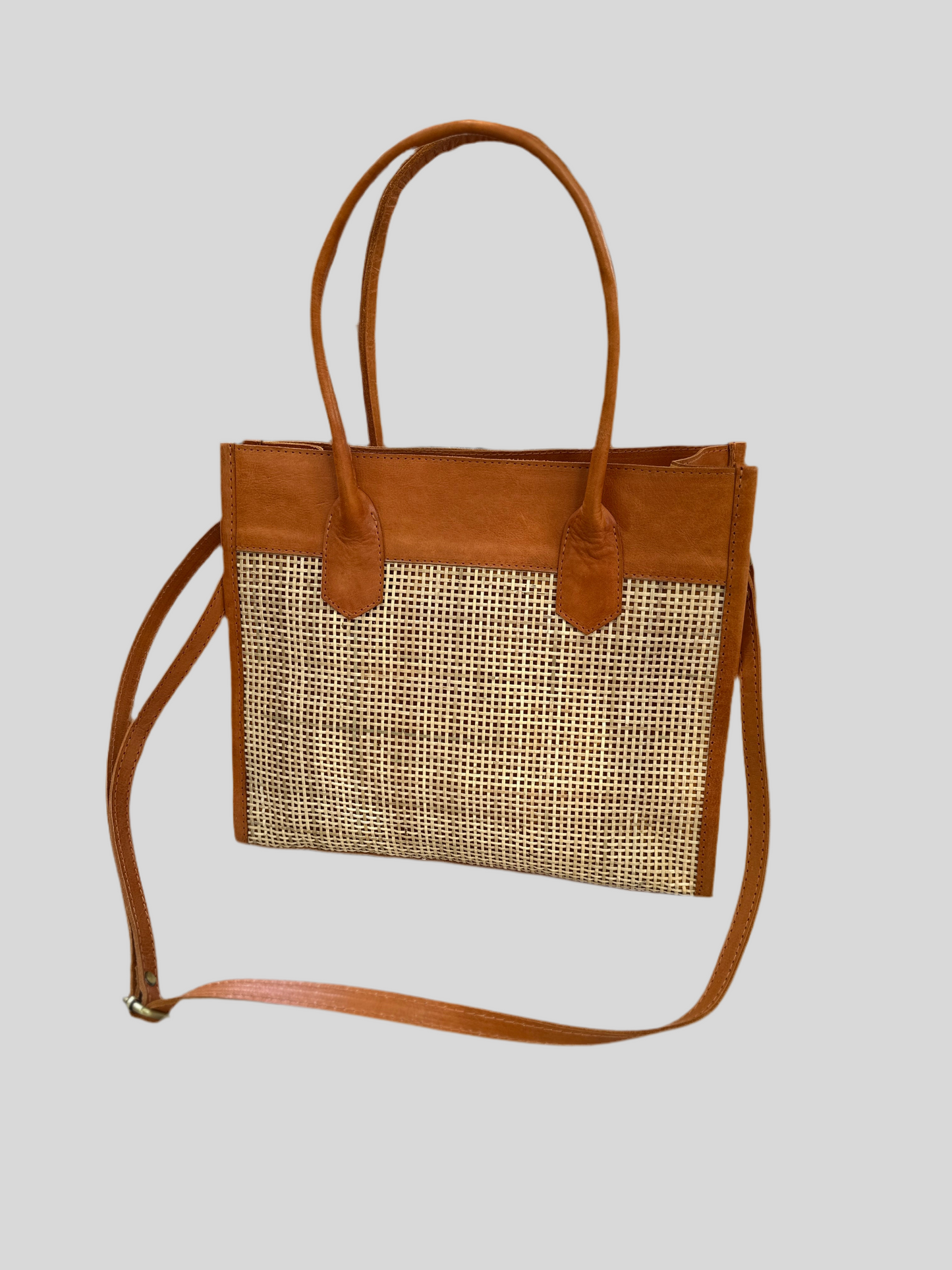 Rome Rattan Handbag in tan cowhide leather and natural rattan with dual handles, adjustable crossbody strap, small interior pocket, and secure zipper closure. Lightweight, compact, and perfect for everyday elegance.
