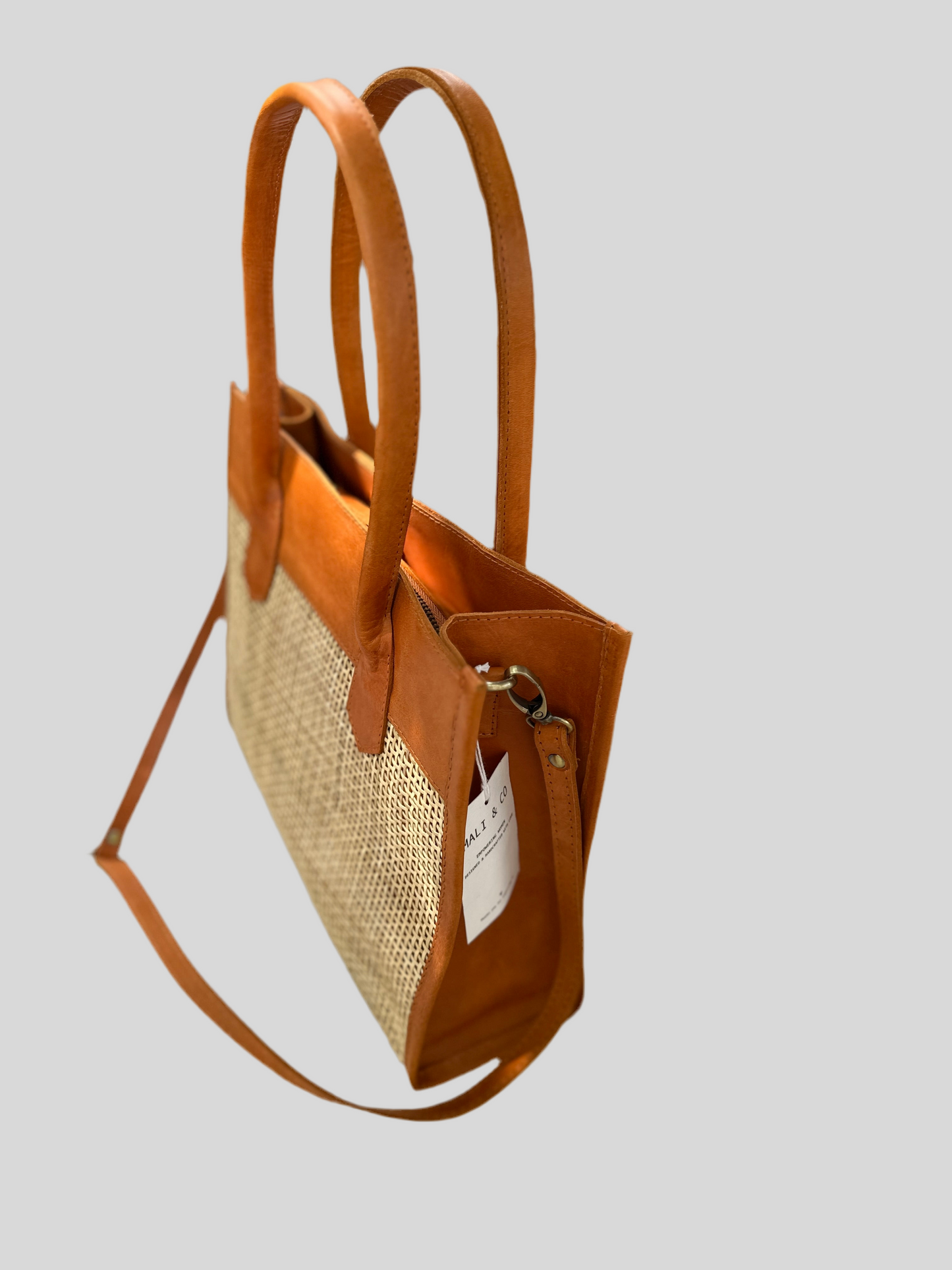 Rome Rattan Handbag in tan cowhide leather and natural rattan with dual handles, adjustable crossbody strap, small interior pocket, and secure zipper closure. Lightweight, compact, and perfect for everyday elegance.