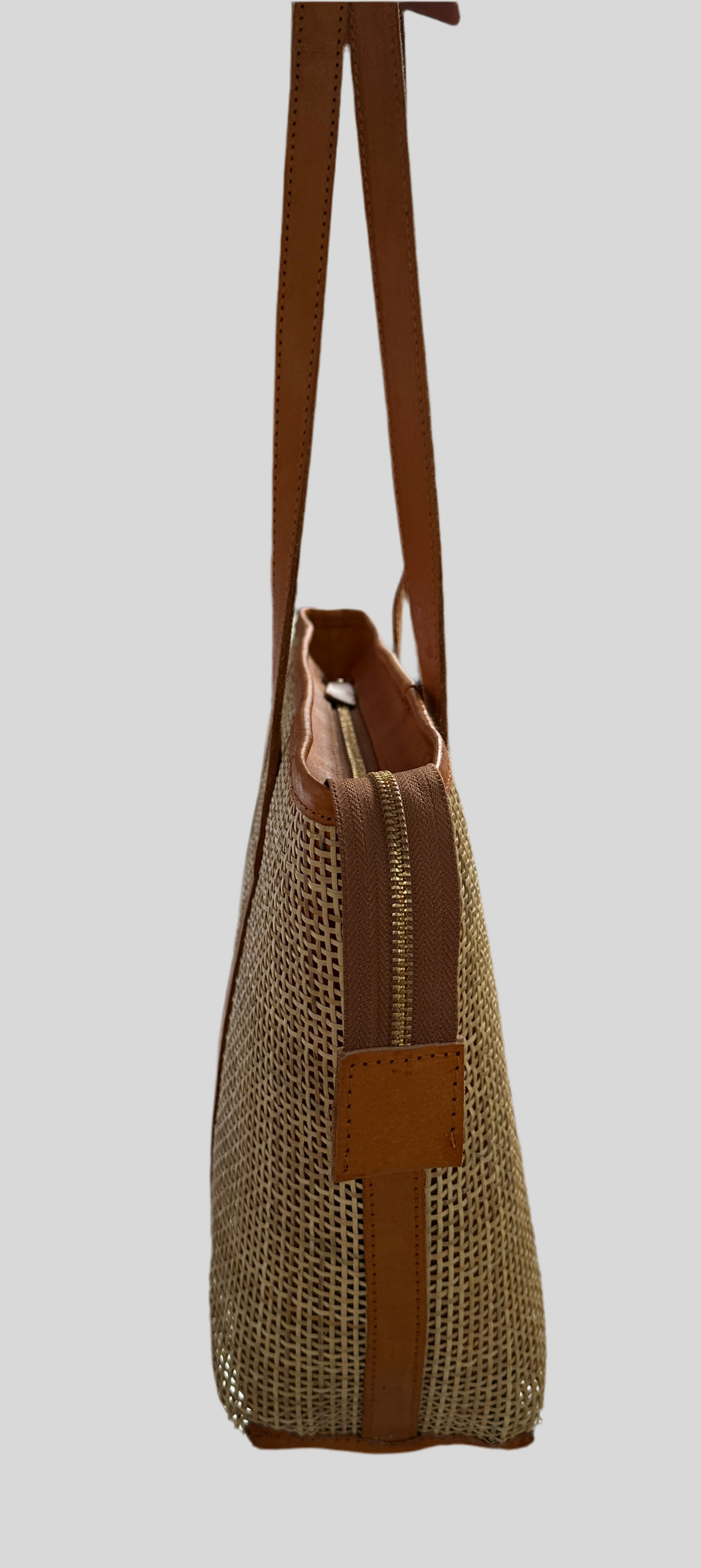 Side view of the Handcrafted Capri rattan tote bag with tan leather straps and natural rattan body. Features secure zipper closure and spacious interior for work or casual use.